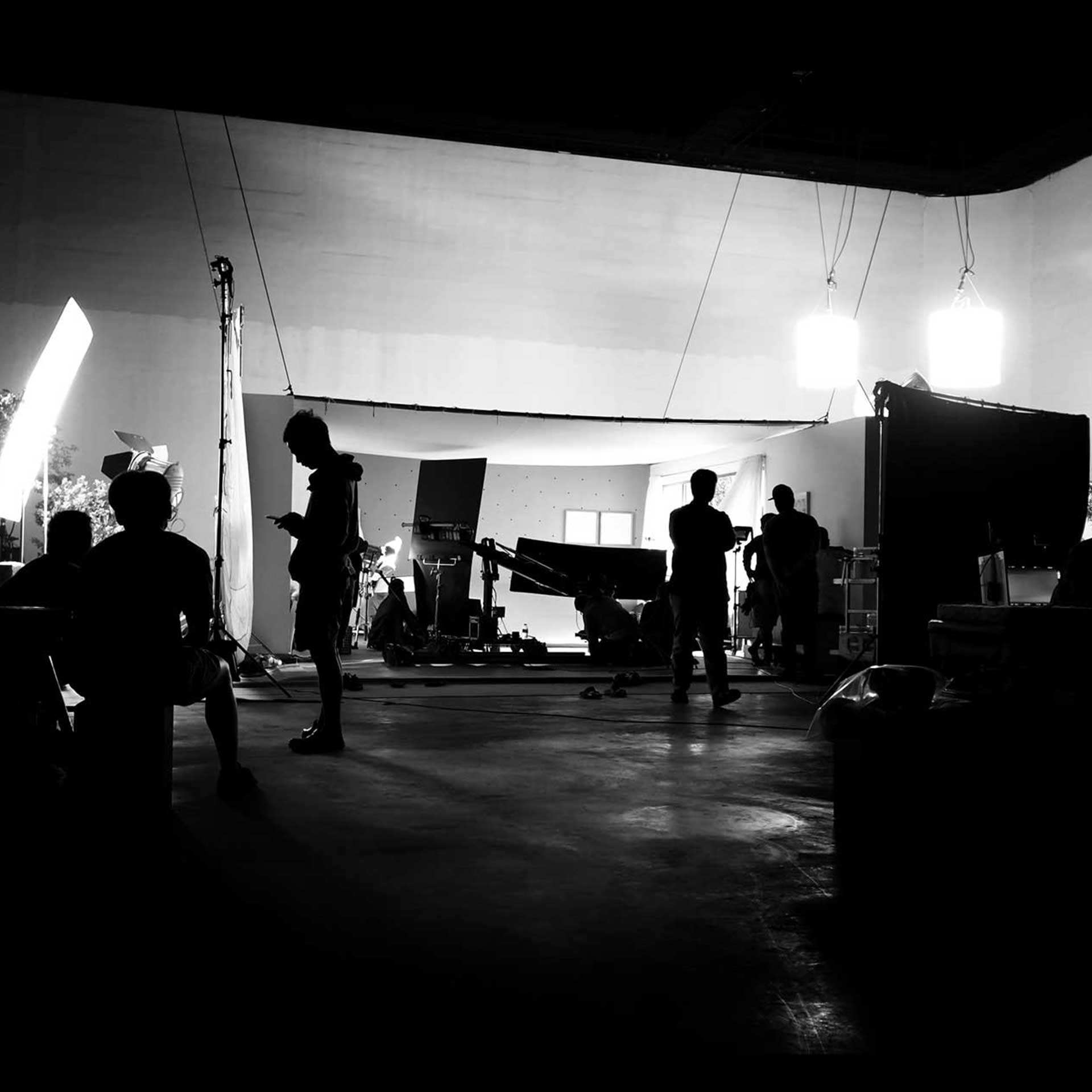 People work on a film set with lighting equipment, cameras, and crew visible in silhouette against a bright backdrop, efficiently coordinating tasks much like Benefit Administration Services streamline workplace operations.