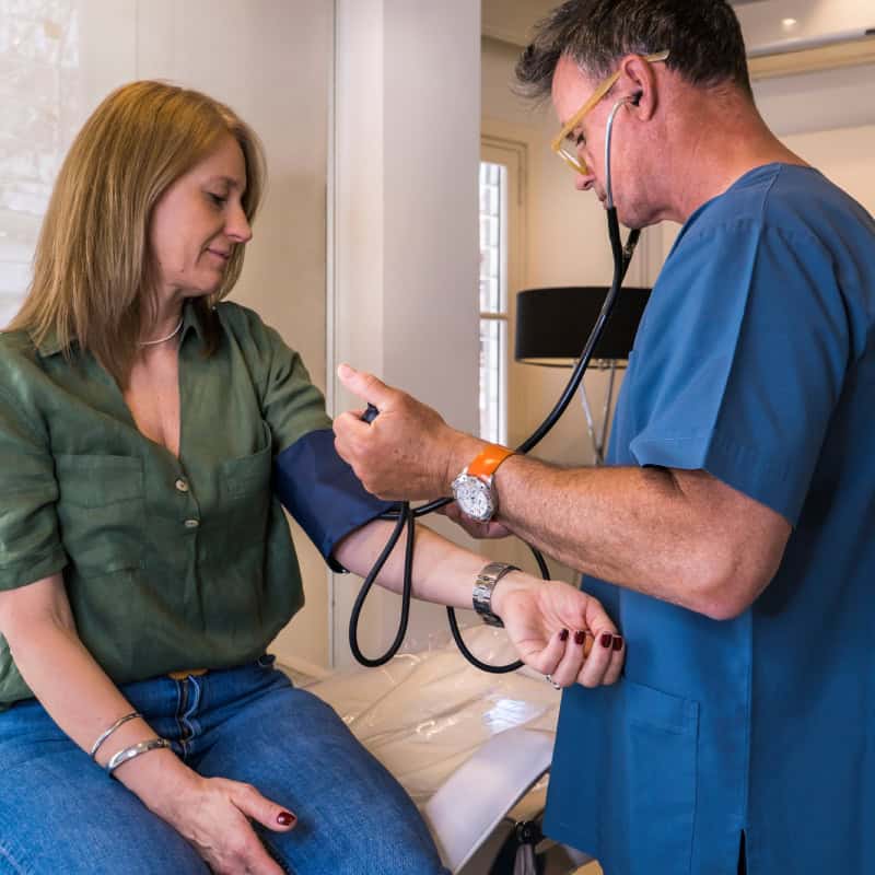 A healthcare professional measures a woman's blood pressure using a cuff and stethoscope during a medical examination.