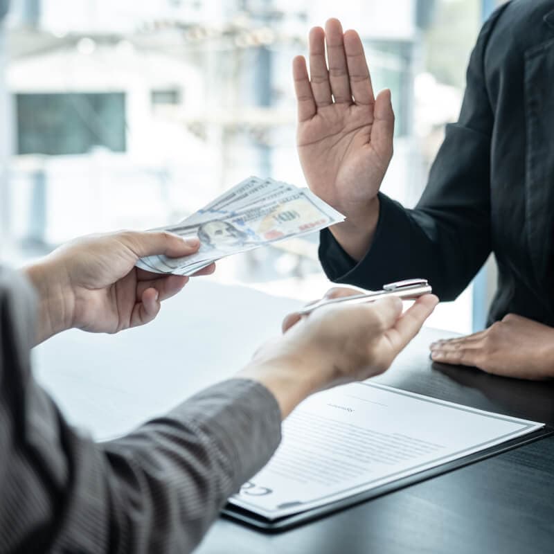 A person refuses an offered stack of cash while another hand holds a pen near a document on a table.